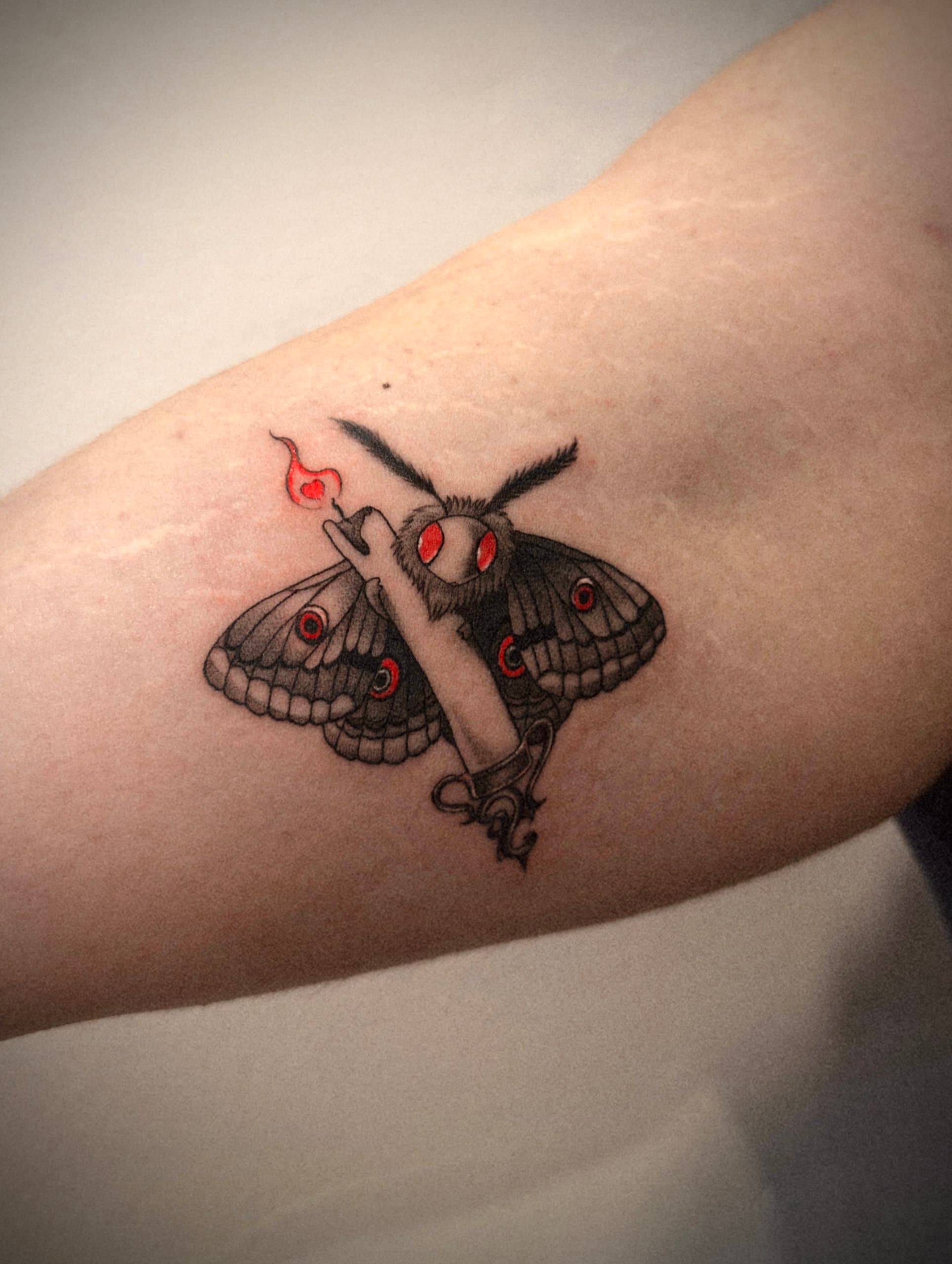 Illustrative moth and candle tattoo in black and red ink
