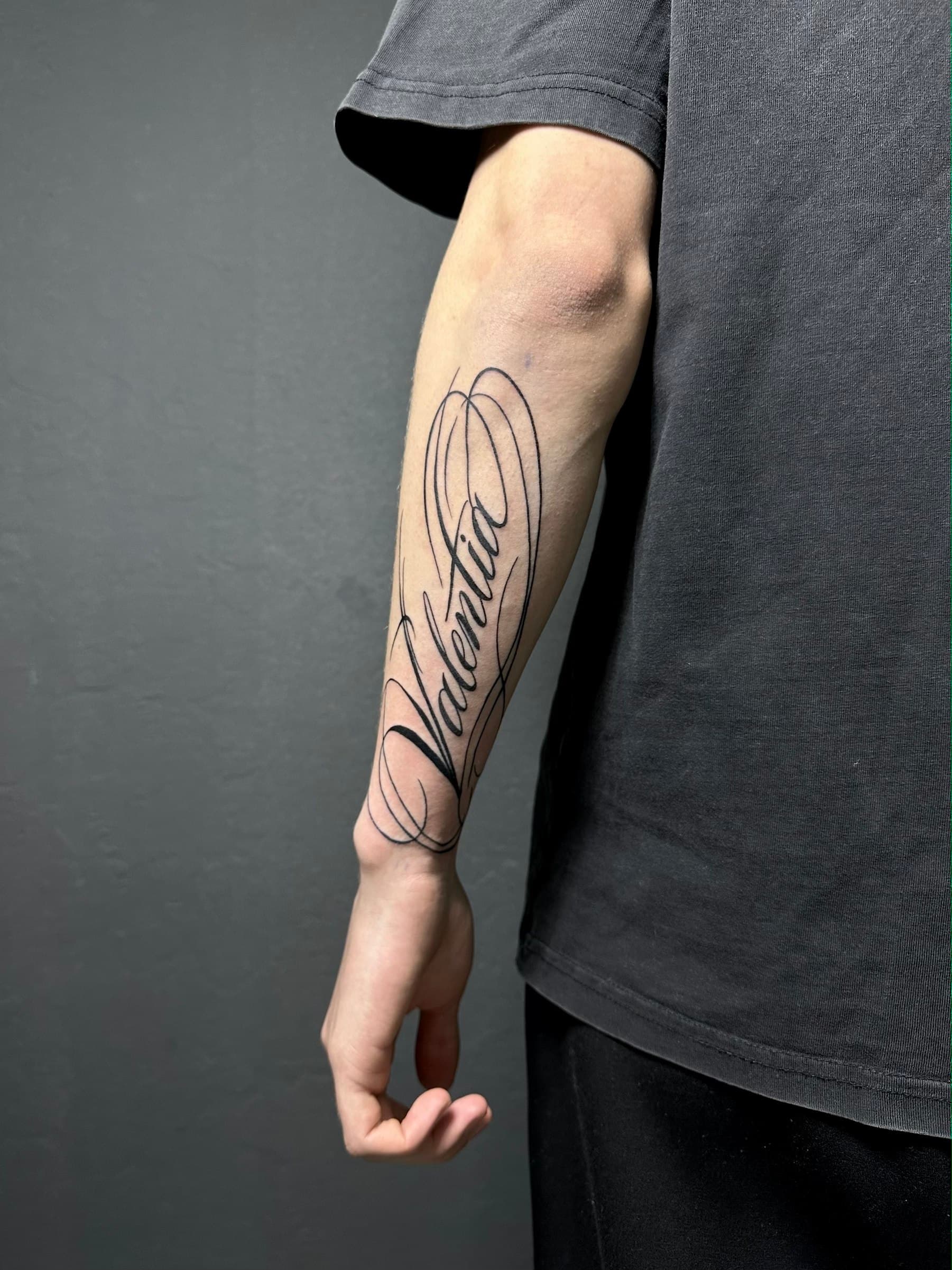 Flowing calligraphy lettering tattoo on the forearm