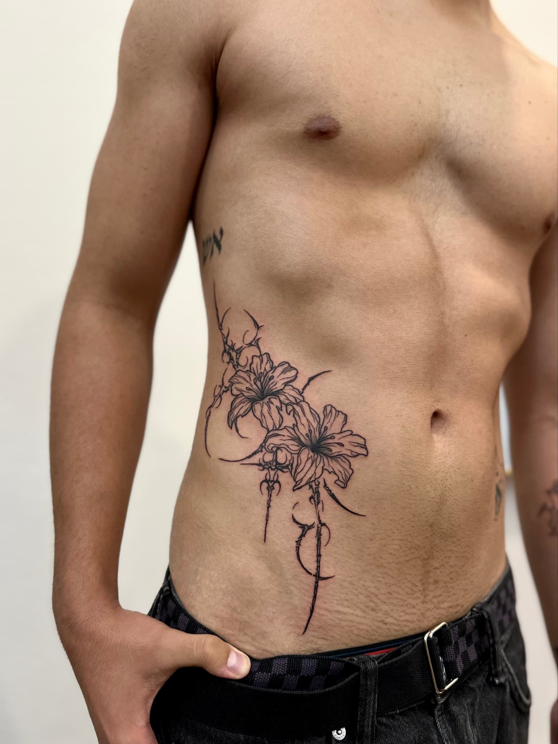 Fine line lily tattoo with ornamental thorns on the ribs, made at LUX INK Batumi